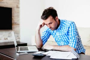 A troubled business owner working on the business' cashflow in his laptop while using calculator and tracking the history of data on the documents