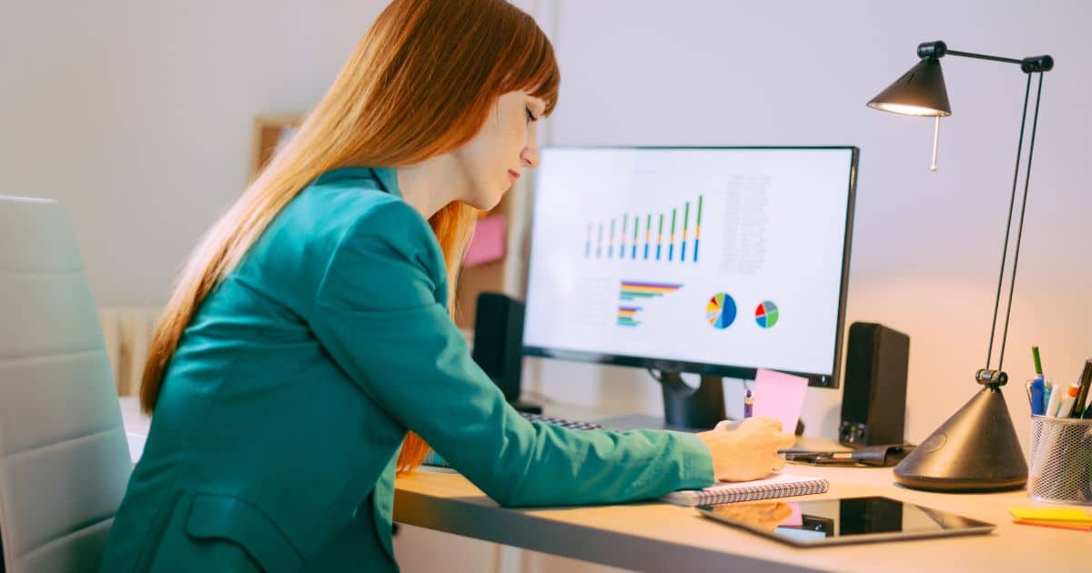 Business Owner writing down the steps on implementing profit share while referencing to the financial data of the company on a computer.