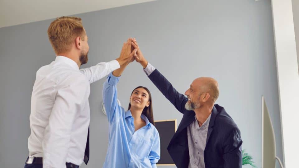 Three business team members raising hands together in showing commitment to the business planning and strategy in an office