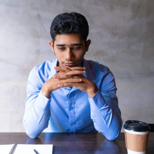 man employee with hands in his chin thinking in a table with notebook and coffee