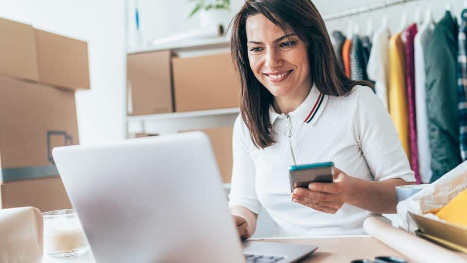 A happy business owner holding a phone on her hand while typing in her laptop