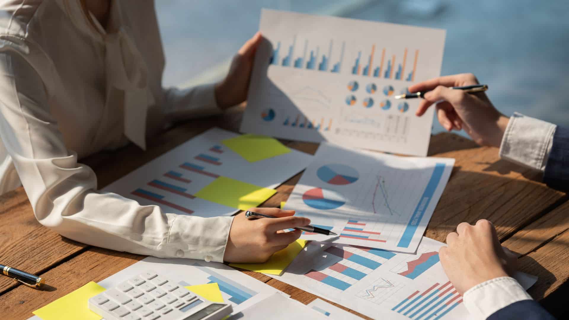 half body of a woman business coach sitting in a table with charts discussing strategy with a business owner