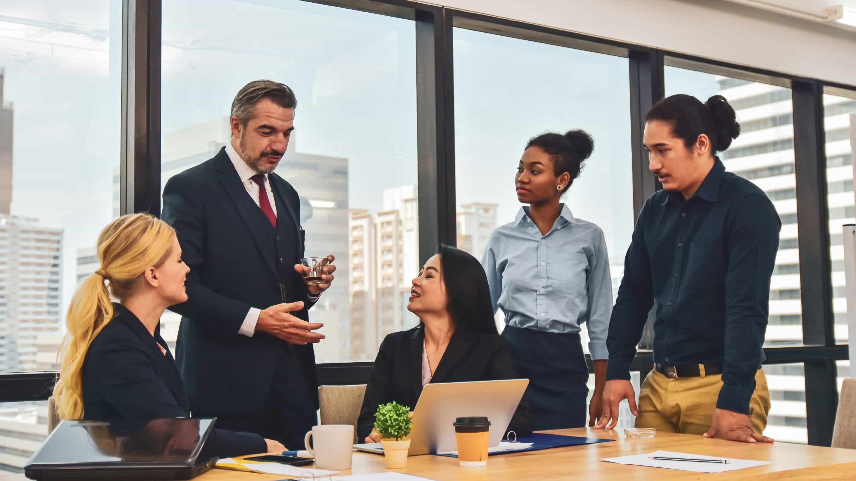 leadership a business leader man holding a cup surrounded by his 4 staff in an office talking