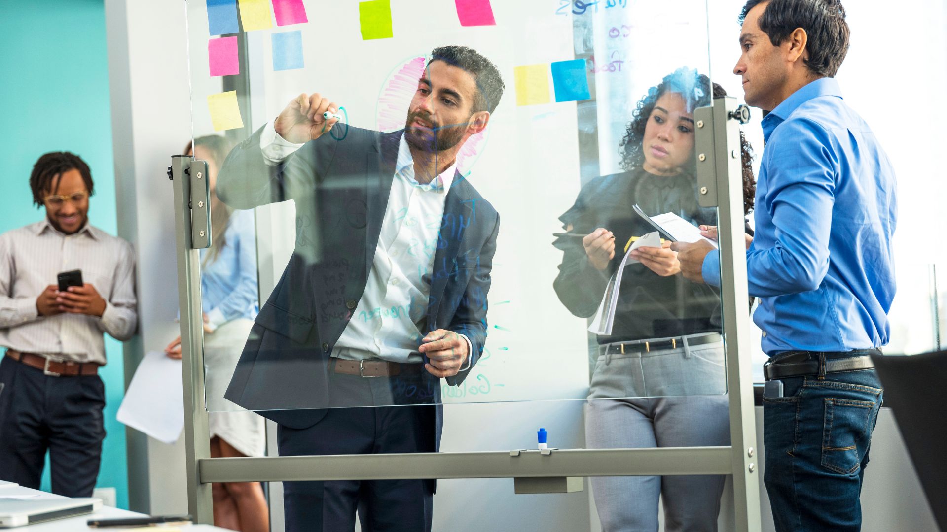 a business leader man holding a cup surrounded by his 4 staff in an office talking